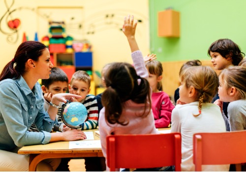 Children in preschool in Peoria IL raising their hand to answer a question