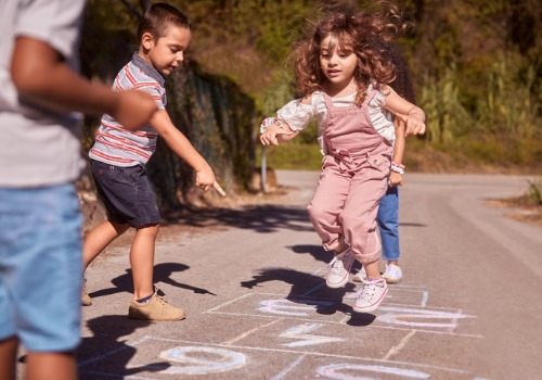 A girl plays hopscotch while other children watch. Setting up playdates is a great way to ease back to school anxiety for kids.