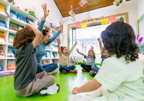 Toddlers and their teacher laugh with their hands in the air at PALS, a Child Care Center by Peoria County IL