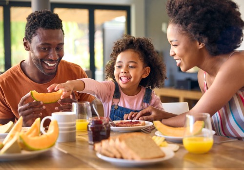 Parents and their young daughter enjoy a balanced meal together at breakfast, which is a great way to encourage Healthier Eating Habits in Kids.