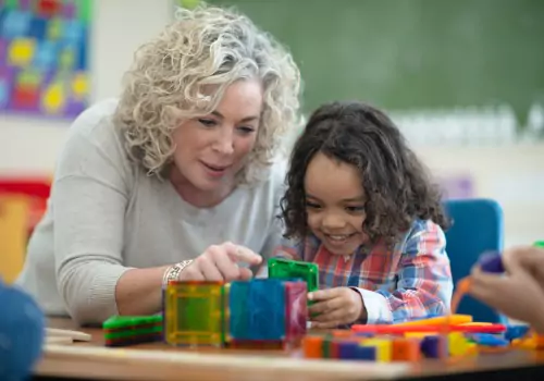 A preschool teacher works hands-on with a child to model behaviors, which is one of the ways how PALS instructs your children.