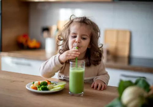 A child drinks a smoothie and snacks on fresh vegetables, which is a great way to establish Healthy Habits for a New Year.
