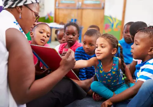 A teacher reads a book with a class of preschool kids, which is one of the researched ways for how PALS instructs your children.