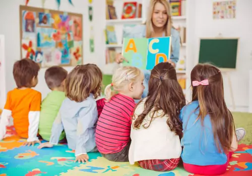 Women reading the alphabet book to six children in a classroom at the best preschool in Peoria IL.