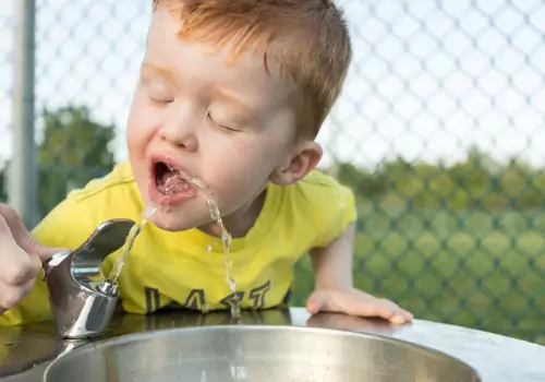 A boy drinks water from a water fountain. Keeping hydrated is one of the top Outdoor Safety Tips for Kids to learn.