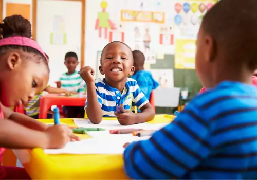 A boy smiles at the camera while doing crafts, which is an excellent option for Summertime Activities for Kids