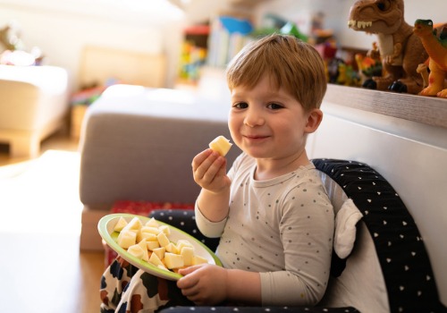 A toddler snacks on apples as part of a snack time option to build in regular routines during the holidays
