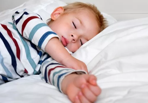 A child sleeps in bed to keep nap time consistent as part of a Snow day Survival Guide