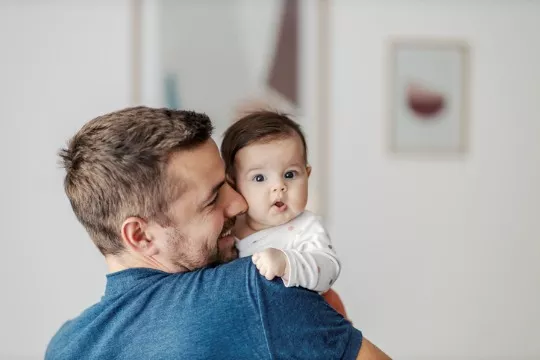A happy father holds his baby while she looks at the camera at the end of the day where she was part of the PALS infant program