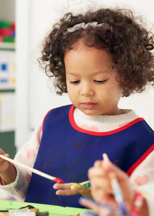A girl in the PALS toddler program paints during craft time in the classroom