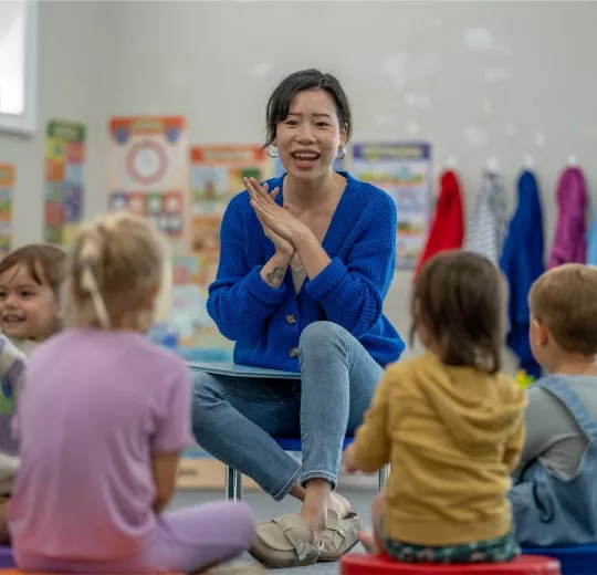 A teacher from PALS’ Pre-K Program sits in front of her students, on the floor of the classroom as she prepares to read them a story.
